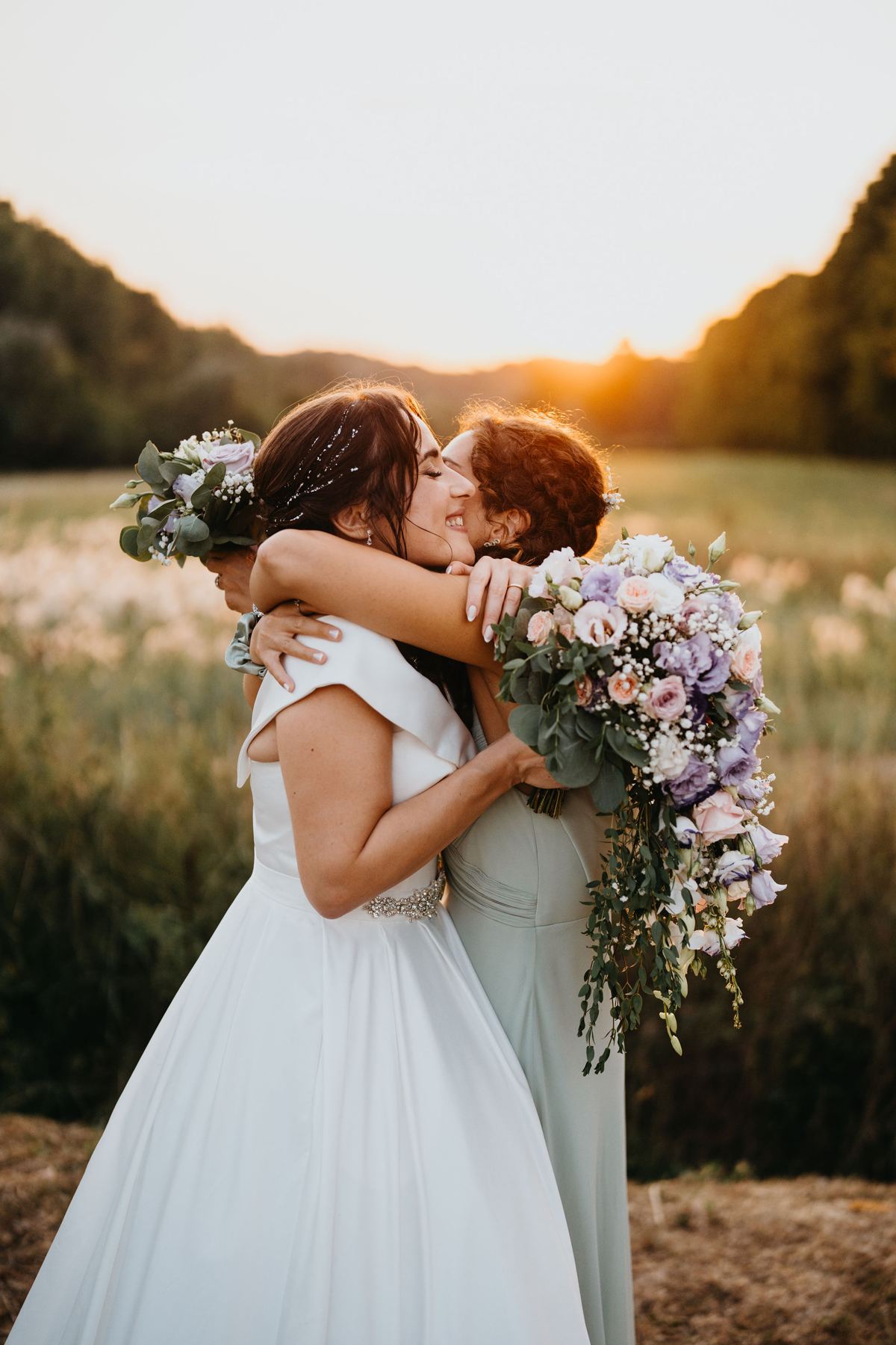 Sposa abbraccia un'amica al tramonto con il bouquet in mano